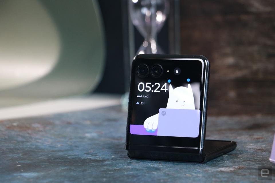 <p>The Motorola Razr+ half folded and propped up on a surface with its front screen facing out. On the display is a wallpaper featuring a cartoon polar beat, the clock widget and small icons indicating the weather.</p>
