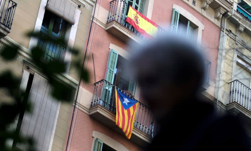 FILE PHOTO: Woman walks past an Estelada (Catalan separatist flag) and a Spanish flag hanging on balconies in Barcelona