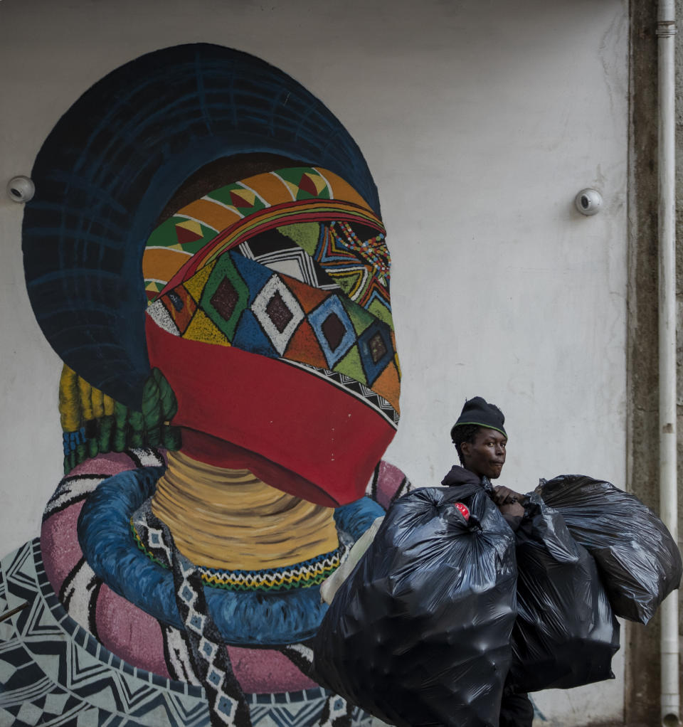 A man carrying plastic bags walks past a mural outside the Wits University school of art in Johannesburg, South Africa, Monday, March 16, 2020. South African President Cyril Ramaphosa declared a national state of disaster. Ramaphosa said all schools will be closed for 30 days from Wednesday and he banned all public gatherings of more than 100 people. South Africa will close 35 of its 53 land borders and will intensify screening at its international airports. For most people, the new COVID-19 coronavirus causes only mild or moderate symptoms. For some it can cause more severe illness. (AP Photo/Themba Hadebe)