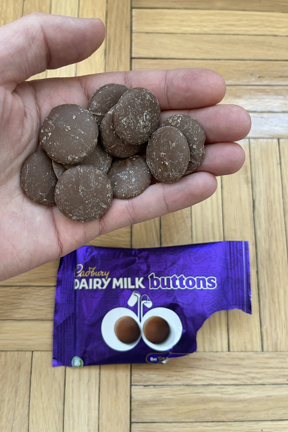 Hand holding Cadbury Dairy Milk Buttons with open packaging below