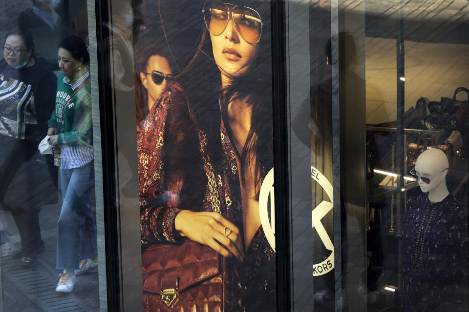 Shoppers, some wearing a face mask to help curb the spread of the coronavirus are reflected on a fashion boutique's window panel as they walk through the capital city's popular shopping mall in Beijing, Monday, Oct. 19, 2020. China’s shaky economic recovery from the coronavirus pandemic is gaining strength as consumers return to shopping malls and auto dealerships while the United States and Europe endure painful contractions. (AP Photo/Andy Wong)