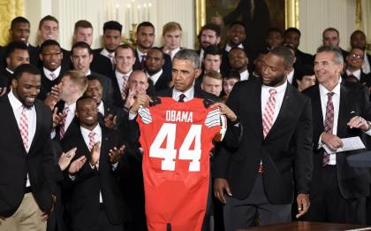 President Barack Obama holds up a Ohio State football jersey that he was presented with from Ohio State football players Curtis Grant and Doran Grant, as head coach Urban Meyer watches at right. (AP Photo/Susan Walsh)