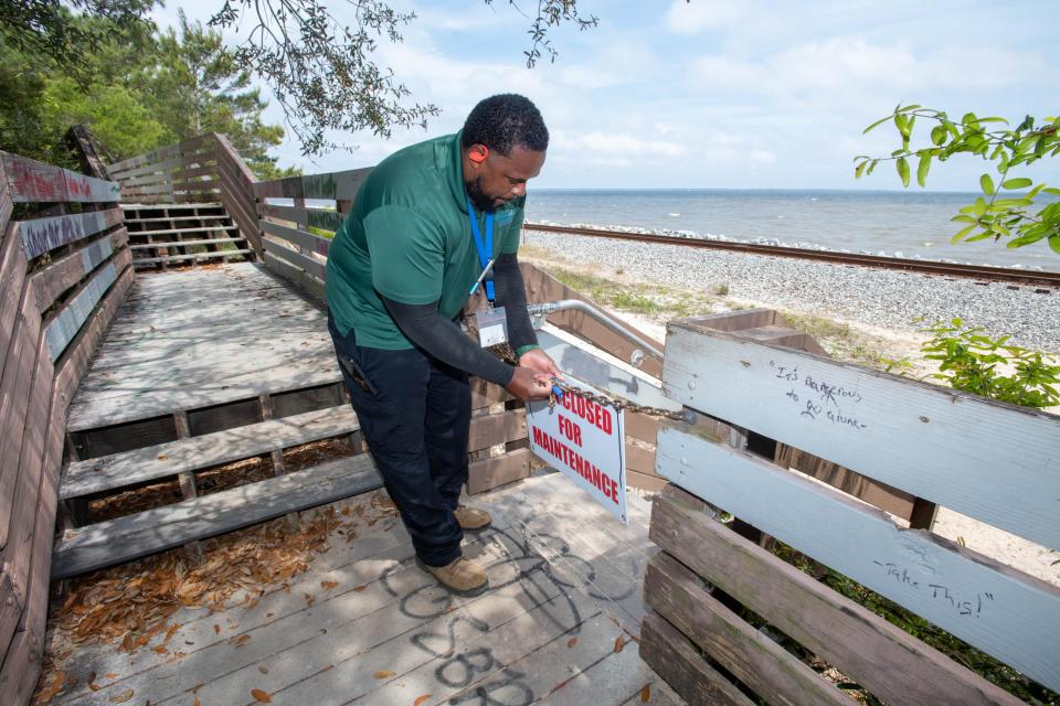 Antonio Shoemaker of Public Works & Facilities locks a chain across an entrance to the boardwalk at Bay Bluffs Park, which is temporarily closed due to its deteriorating condition.