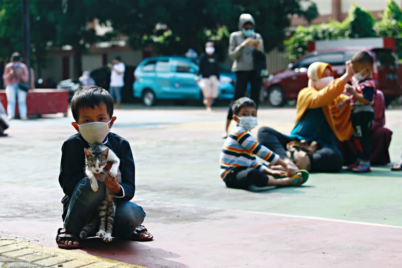 A young boy holds a cat as he waits to take a swab sample to test for the coronavirus disease (COVID-19) during mass testing at a school in Jakarta
