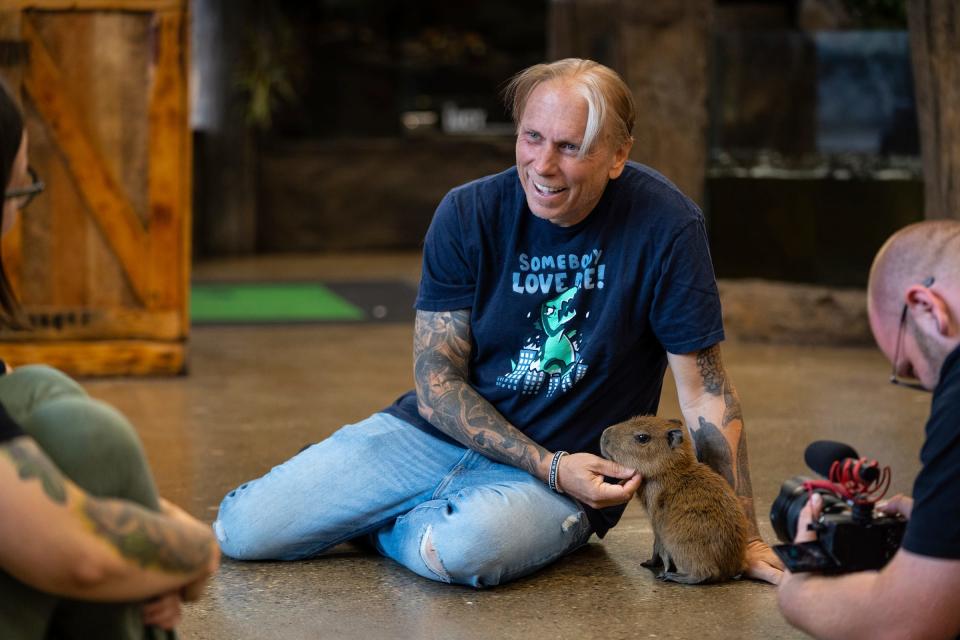 The Reptarium owner Brian Barczyk, center, talks with animal educator Amy Karjala, left, as he holds a Capybara, a new addition to his business, in Utica on Friday, June 23, 2023, as creative director Jay Tomsky films him for their vlog.