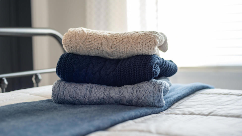 Stack of cable knit sweaters folded on the bed in morning light - Image.