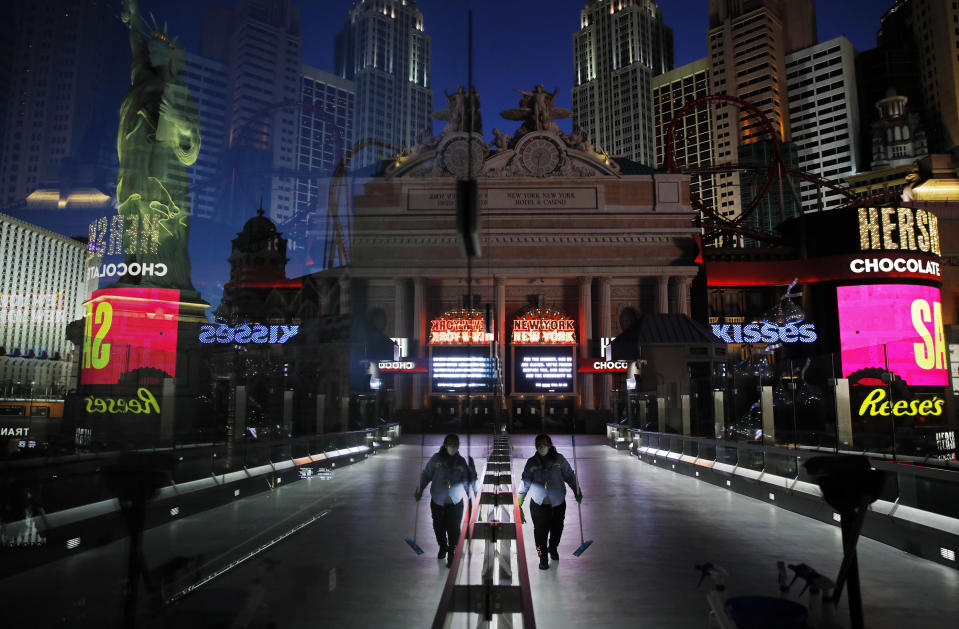 In this April 18, 2020, photo, a lone worker wearing a mask cleans a pedestrian walkway devoid of the usual crowds as casinos and other business are shuttered due to the coronavirus outbreak in Las Vegas. Nevada's governor closed the glitzy casinos and nightlife attractions in mid-March, leaving much of the famous gambling mecca empty, barricaded and abandoned. (AP Photo/John Locher)