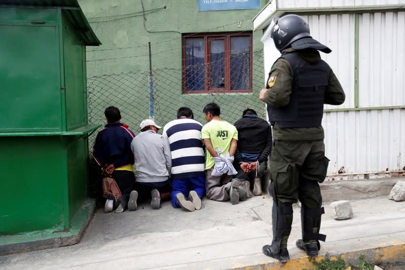 A police officer stands next to people detained during clashes between supporters of Bolivian President Evo Morales, who announced his resignation on Sunday, and opposition supporters in La Paz