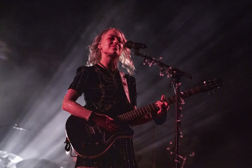 A woman playing guitar and standing in front of a microphone on a stage