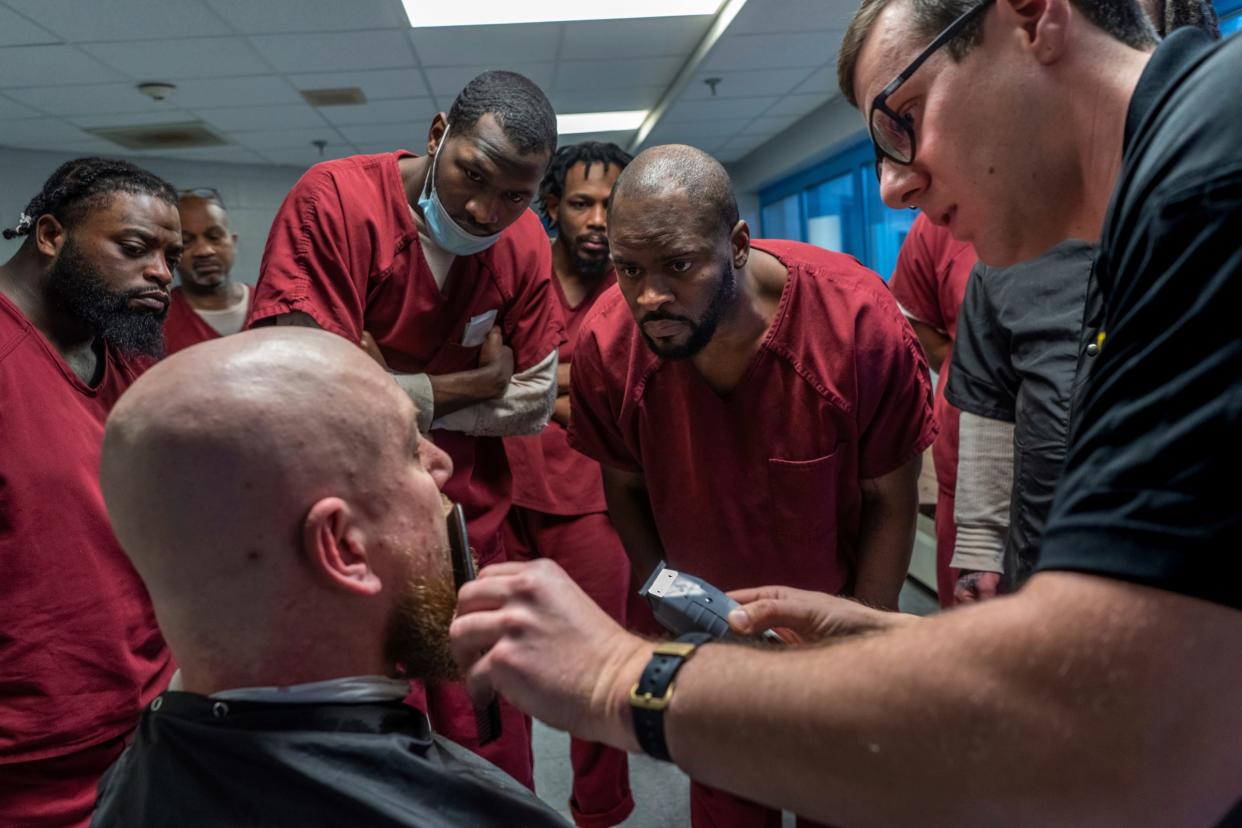 Amier Hill, left, Calvin Robinson and Calvin Clark lean in to get a better view as deputy Nathaniel Minard shows a technique to the class while cutting the beard of James Wheeler during a weekly one-hour barber course for a small group of incarcerated men as part of the I.G.N.I.T.E. (Inmate Growth Naturally and Intentionally Through Education) program held in an activities room of the Genesee County Jail in Flint on Thursday, Jan. 4, 2024. Minard invited Hill and Clark to join the class for the day who had already graduated to help give tips and mentor others involved with their experience cutting hair for almost 10 years before ending up in the jail.