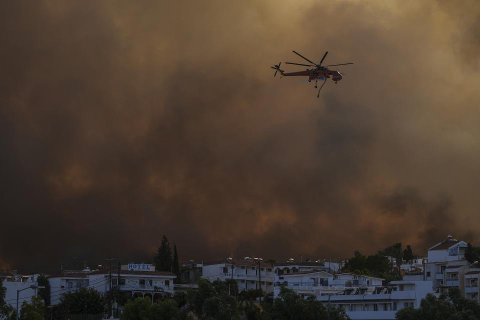 An helicopter operates over a wildfire burning in Gennadi village, on the Aegean Sea island of Rhodes, southeastern Greece, on Tuesday, July 25, 2023. A firefighting plane has crashed in southern Greece, killing both crew members, as authorities are battling fires across the country amid a return of heat wave temperatures. (AP Photo/Petros Giannakouris)
