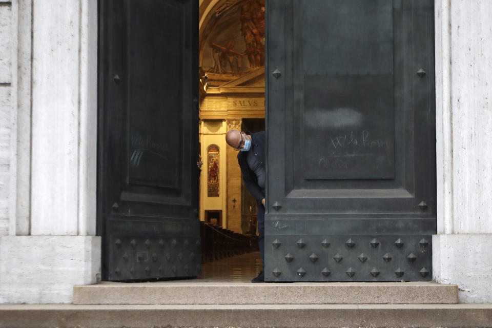 Father Jose Maria Galvan, wearing a sanitary mask to prevent the spread of COVID-19 opens the door for the morning mass at St. Eugenio Church, in Rome, Monday, May 18, 2020. Italy partially lifted sanitary restrictions Monday after a two-month coronavirus lockdown. (AP Photo/Alessandra Tarantino)