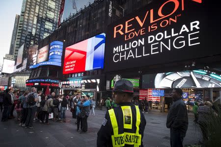 A Public Safety officer keeps watch as people stand in front of a billboard owned by Revlon that takes their pictures and displays them in Times Square in the Manhattan borough of New York October 13, 2015. REUTERS/Carlo Allegri