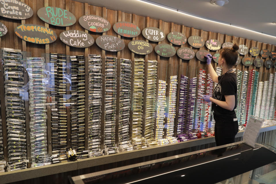 In this photo taken March 24, 2020, budtender Maegan Clark writes on a sign at the pre-roll area of The Reef Capitol Hill, a marijuana store in Seattle. Earlier in the week, Washington Gov. Jay Inslee ordered nonessential businesses to close and the state's more than 7 million residents to stay home in order to slow the spread of the new coronavirus. In Washington and several other states where marijuana is legal, pot shops and workers in the market's supply chain were deemed essential and allowed to remain open. Signs posted at the store said that The Reef is donating 5% of its profits to Seattle-area coronavirus relief efforts. (AP Photo/Ted S. Warren)