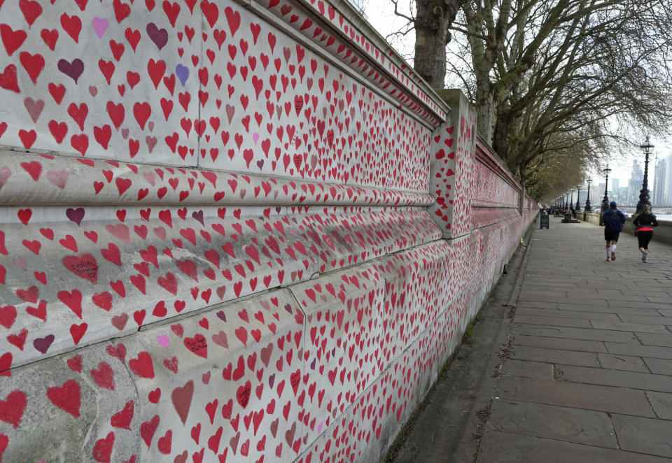 People jog past the 'The National COVID Memorial Wall' on the south bank of the Thames in front of St. Thomas' hospital and opposite the House of Parliament in London, Sunday April 4, 2021. Hearts are being drawn onto the wall in memory of the many thousands of people who have died in the UK from coronavirus, with organizers hoping to reach their target of 150,000 hearts by the middle of next week. (AP Photo/Tony Hicks)