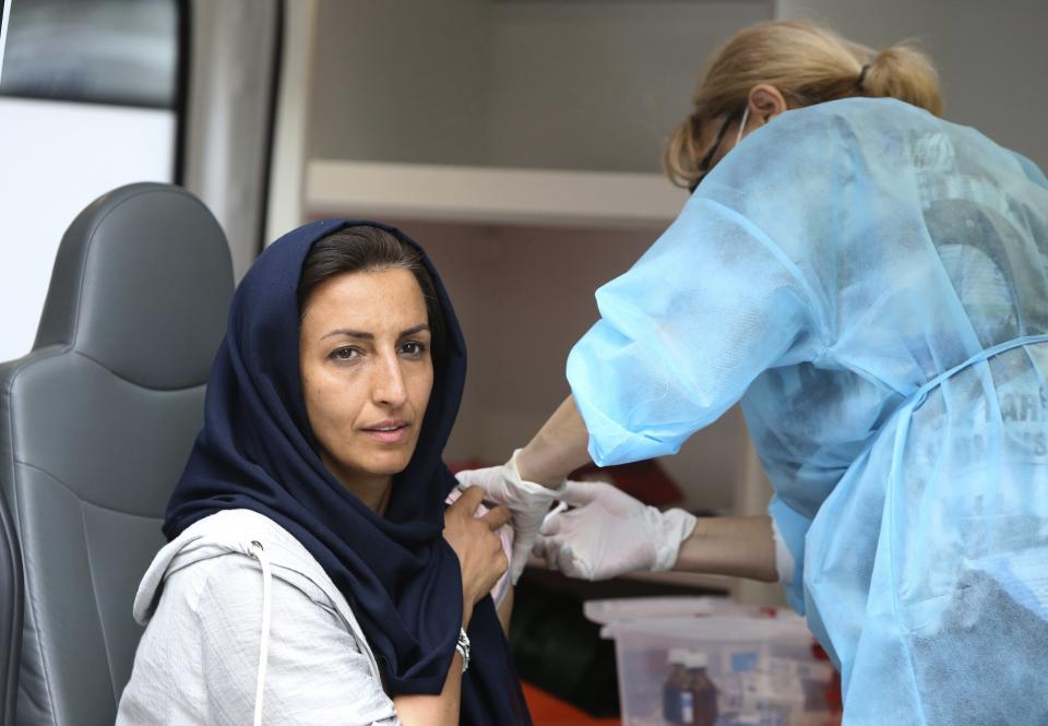 A woman gets a shot of coronavirus vaccine at a mobile vaccination station in the center of Yerevan, Armenia, Wednesday, July 14, 2021. Some hundreds lined the streets of the Armenian capital to get free coronavirus shots, and some spent night on the streets to save on queueing. Under the Armenian government's directives effective since Friday, foreign nationals can only get AstraZeneca shots at five mobile vaccination points in Yerevan. (Vahram Baghdasaryan/PHOTOLURE via AP)