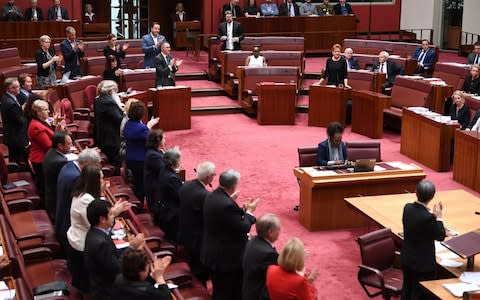 Senators from both sides join in applauding Attorney-General George Brandis (unseen) for criticising One Nation Senator Pauline Hanson - Credit: AAP