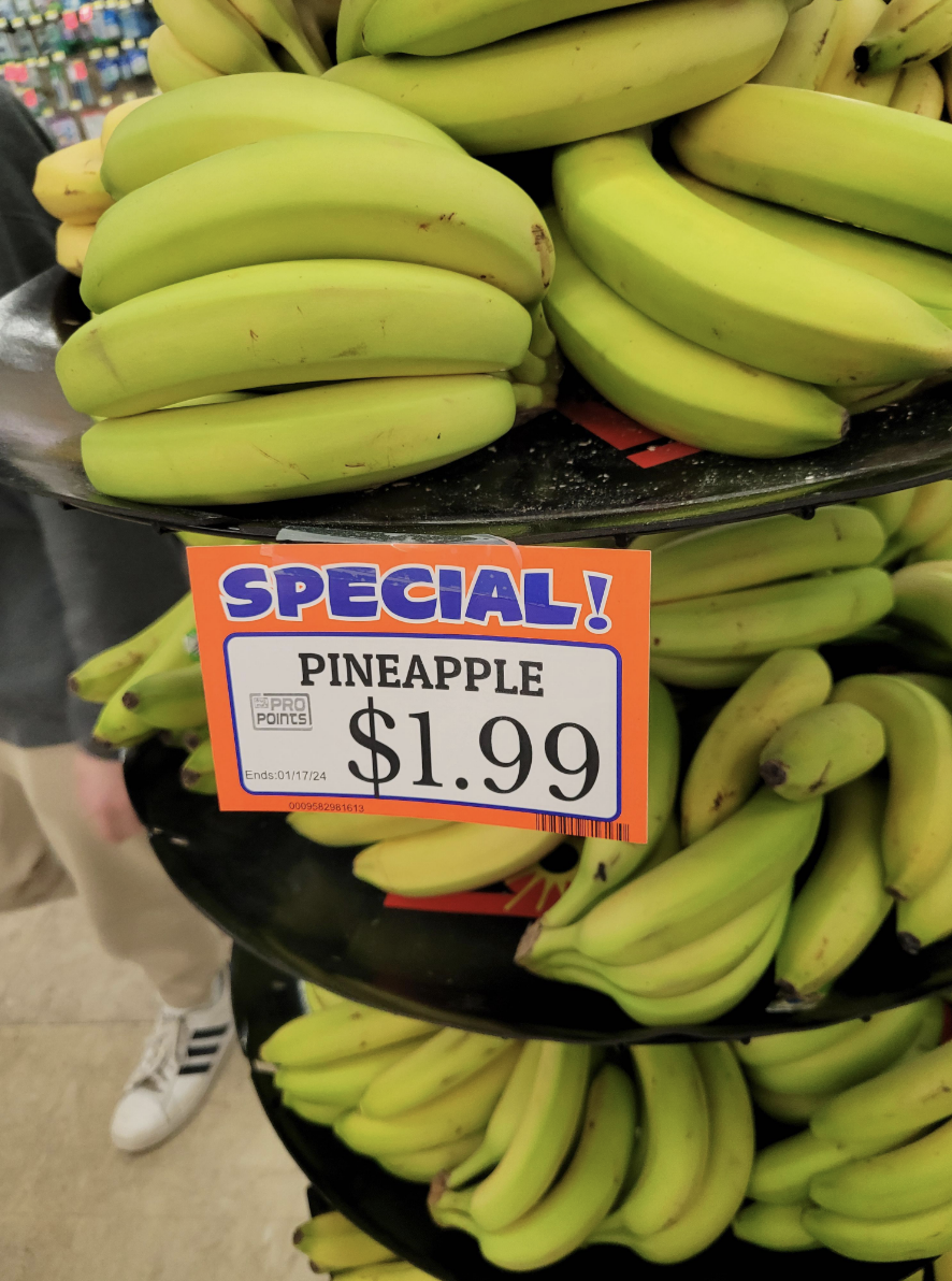 Bunches of bananas in the store with a "Pineapple $2" sign