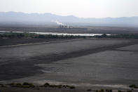 A dried up portion of the Salton Sea stretches out with a geothermal power plant in the distance in Niland, Calif., Thursday, July 15, 2021. Demand for electric vehicles has shifted investments into high gear to extract lithium from geothermal wastewater around the rapidly shrinking body of water. The ultralight metal is critical to rechargeable batteries. (AP Photo/Marcio Jose Sanchez)