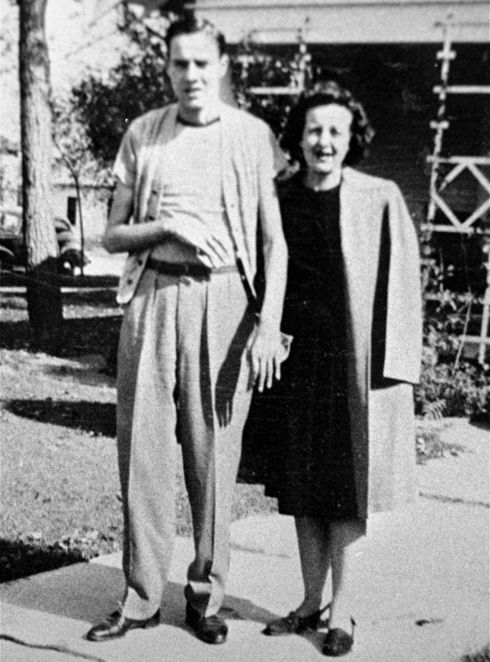 A black-and-white photo of Bob Dole and his mother, Bina, standing in front of the family home.