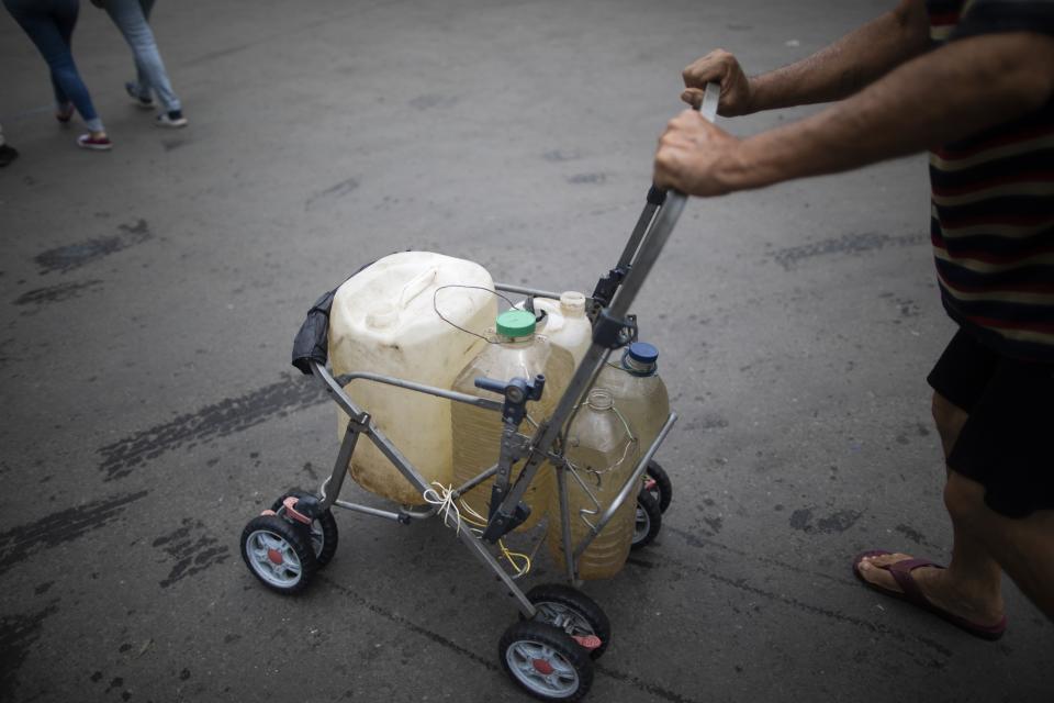 A man pushes a stripped down baby stroller with containers he filled with water that he collected from a street faucet, in Caracas, Venezuela, Saturday, June 20, 2020. Water service in Venezuela has gotten so bad that poor neighborhoods have started to rig private water systems or hand dig shallow wells. (AP Photo/Ariana Cubillos)