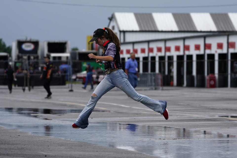 A person leaps across a puddle in the garage area after a rain storm cancelled practice and qualifying for Saturday's NASCAR Truck Series auto race at Pocono Raceway, Friday, July 22, 2022, in Long Pond, Pa. (AP Photo/Matt Slocum)