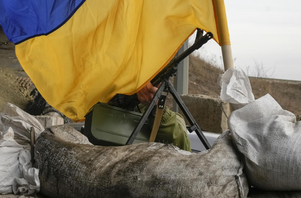 FILE - A machine gun emerges from under the Ukrainian flag on a front line position near Kharkiv, Ukraine, Saturday, March 26, 2022. With its aspirations for a quick victory dashed by a stiff Ukrainian resistance, Russia has increasingly focused on grinding down Ukraine’s military in the east in the hope of forcing Kyiv into surrendering part of the country’s eastern territory to end the war. If Russia succeeds in encircling and destroying the Ukrainian forces in Donbas, the country’s industrial heartland, it could try to dictate its terms to Kyiv -- and possibly attempt to split the country in two. (AP Photo/Efrem Lukatsky)
