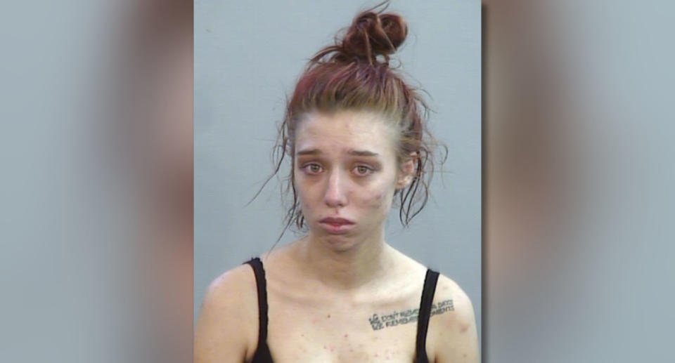 A mugshot of Tiffany-Anne Brislane with a black top, tattoo on left shoulder and dyed red hair.