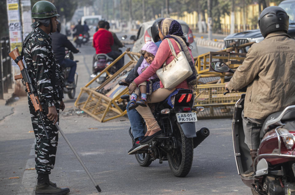 An Indian family rides past police barricades damaged by protestors in Gauhati, India, Thursday, Dec. 12, 2019. Police arrested dozens of people and enforced curfew on Thursday in several districts in India’s northeastern Assam state where thousands protested legislation granting citizenship to non-Muslims who migrated from neighboring countries. (AP Photo/Anupam Nath)