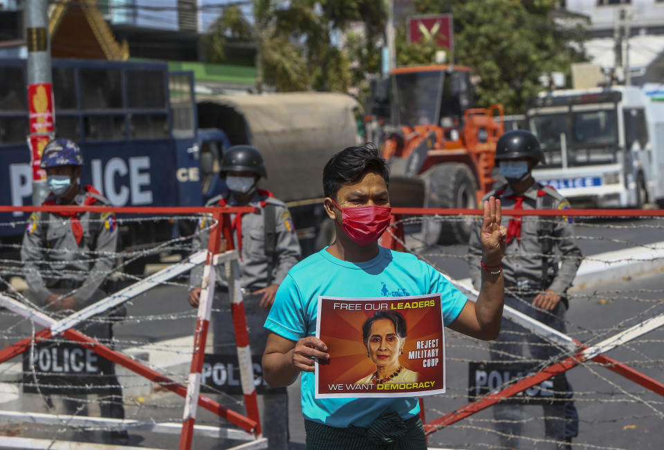 An anti-coup protester flashes the three-fingered salute of defiance as police stand watch in Mandalay, Myanmar, Wednesday, Feb. 24, 2021. Protesters against the military's seizure of power in Myanmar were back on the streets of cities and towns on Wednesday, days after a general strike shuttered shops and brought huge numbers out to demonstrate. (AP Photo)