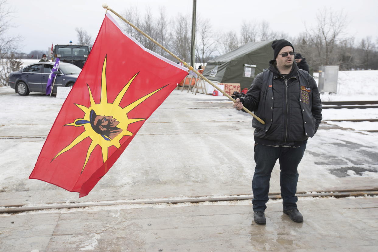 A man holds a warrior flag during the sixth day of blockade of the CN/VIA train tracks in Tyendinaga Mohawk Territory, near Belleville, Ont., on Tuesday, Feb. 11, 2020, in support of Wet'suwet'en's blockade of a natural gas pipeline in northern B.C.  (Lars Hagberg/The Canadian Press via AP)