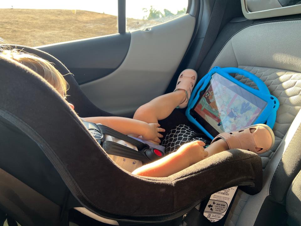 A child sitting in a car seat watching a blue iPad.