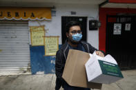 Armando Beltran, 25, whose mother is quarantined in their home with COVID-19 symptoms including fever, headache, exhaustion, and a loss of the sense of smell, carries medical and food supply kits dropped off by city government workers, in the Coyoacan district of Mexico City, Thursday, April 9, 2020. To help halt the spread of the new coronavirus, the Mexican megalopolis is making home deliveries to households with a symptomatic person, providing kits containing food staples, face masks, gloves, antibacterial gel, paracetamol, a thermometer, and benefits cards with a balance of 1000 pesos (around $42). (AP Photo/Rebecca Blackwell)