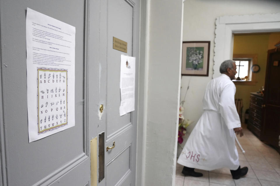 In this Sunday, Dec. 15, 2019, photo, a guide to the alphabet in American Sign Language is taped to a door inside the Holyrood Episcopal Church-Iglesia Santa Cruz in New York. Walking in the background is the Rev. Luis Barrios as he prepares for Spanish-language Mass. (AP Photo/Emily Leshner)