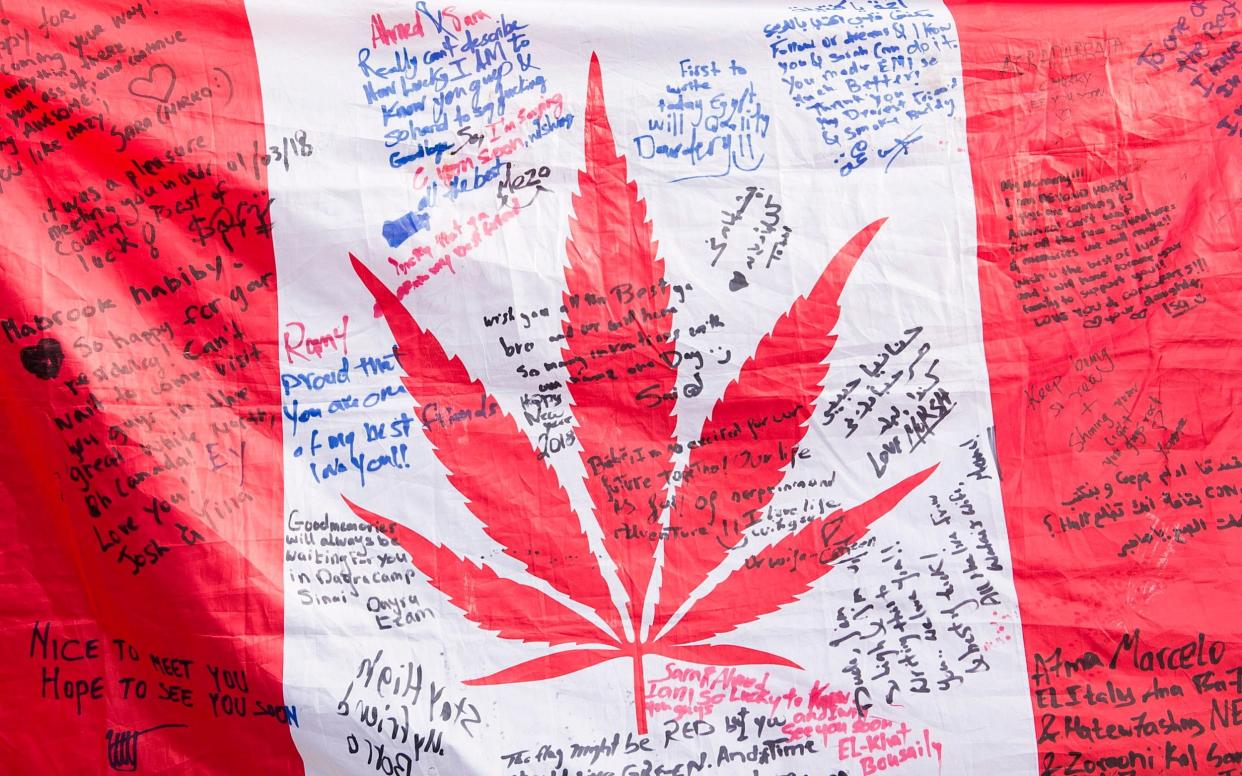 People hold up a Canadian flag with a marijuana logo on it outside a government cannabis store in Montreal - The Canadian Press