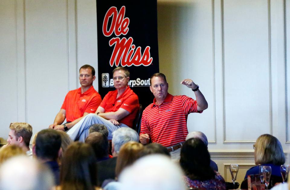 In this Tuesday, July 18, 2017, photo, Mississippi athletic director Ross Bjork, left, and Mississippi Chancellor Jeffrey Vitter listen as football coach Hugh Freeze speaks before alumni and athletic supporters during a Rebel Road Trip visit in Jackson, Miss.