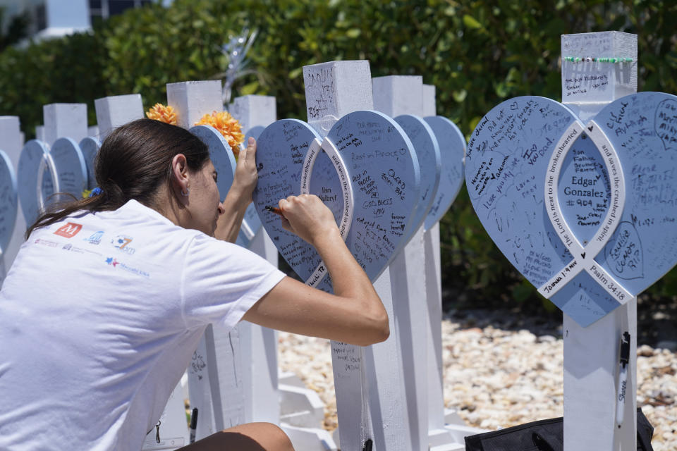 Dalia Gutman, cousin of Ilan Naibryf, writes a message in her cousin's memory during a remembrance event at the site of the Champlain Towers South building collapse, Friday, June 24, 2022, in Surfside, Fla. Friday marks the anniversary of the oceanfront condo building collapse that killed 98 people in Surfside, Florida. The 12-story tower came down with a thunderous roar and left a giant pile of rubble in one of the deadliest collapses in U.S. history. (AP Photo/Wilfredo Lee)