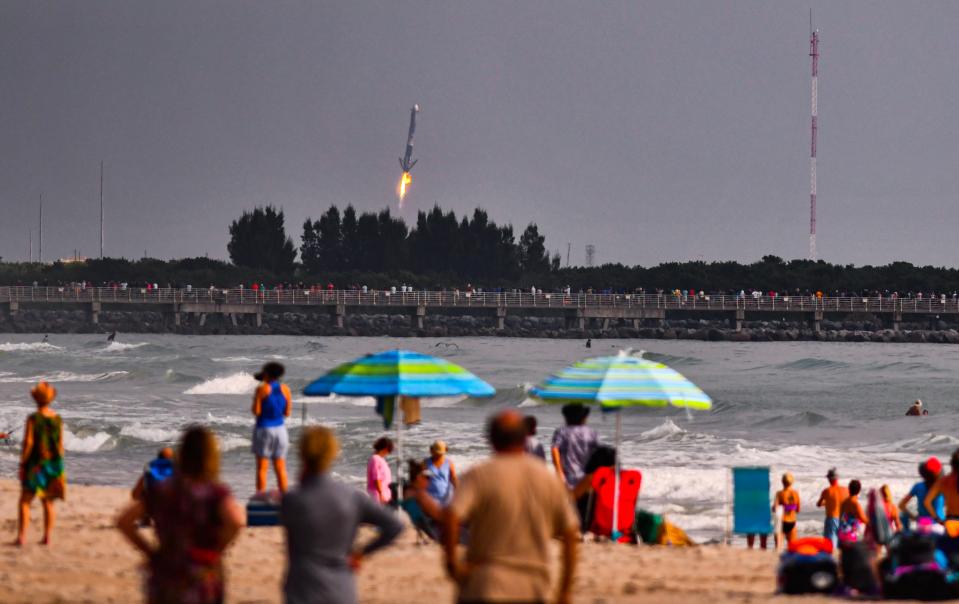 Crowds on the beach in Cape Canaveral watch a SpaceX Falcon Heavy booster land on Oct. 13 at Cape Canaveral Space Force Station about eight minutes after launch.