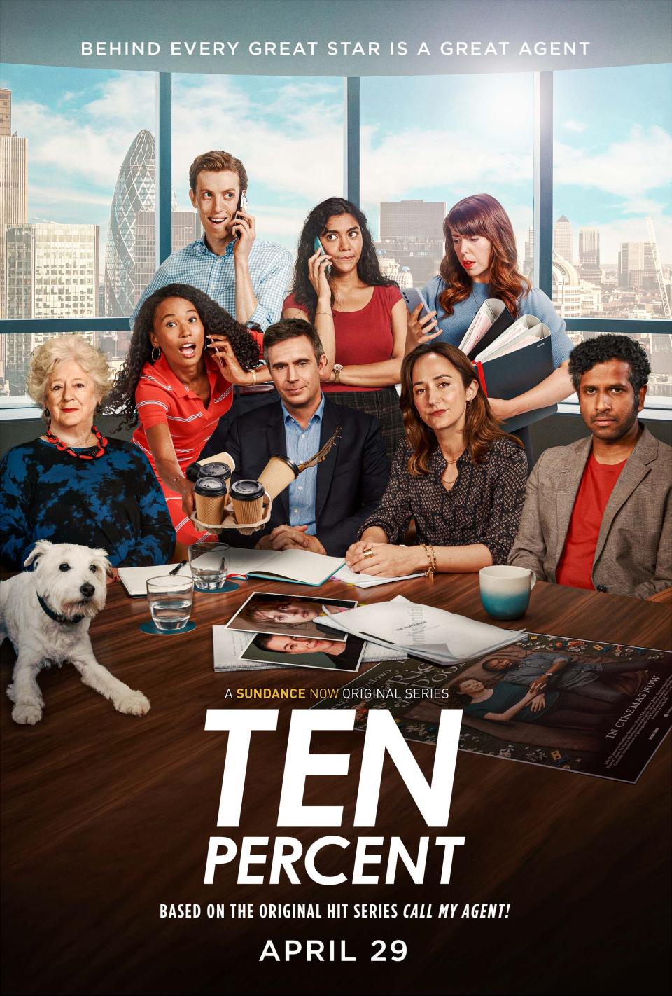 A promotional image from Ten Percent showing a group of people sitting around a table with a city backdrop seen through a window, and a white dog on the table with various photographs of actors scattered.