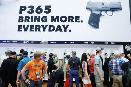 Gun enthusiasts stand below a large handgun advertisement during the annual National Rifle Association (NRA) convention in Dallas, Texas, U.S., May 5, 2018. REUTERS/Lucas Jackson