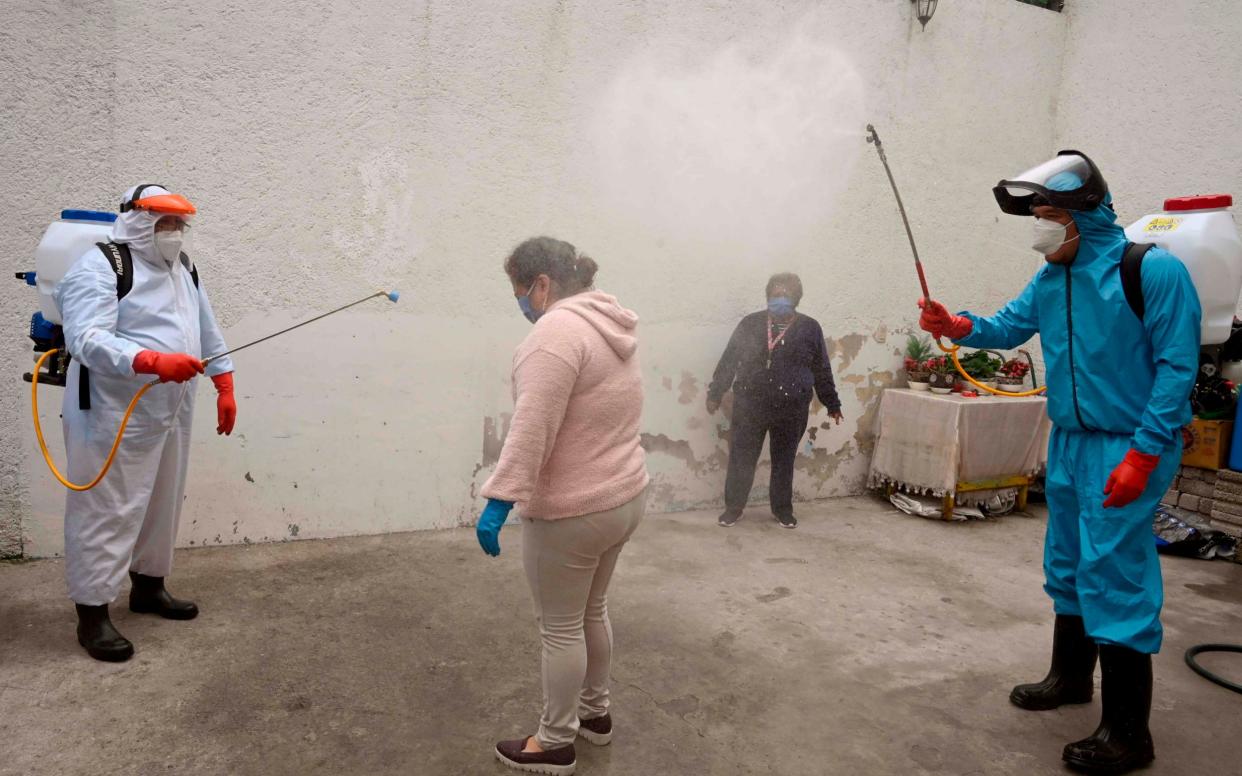 Workers of the Xochimilco local government disinfect a woman and her house as a preventive measure against the spread of the novel coronavirus - AFP
