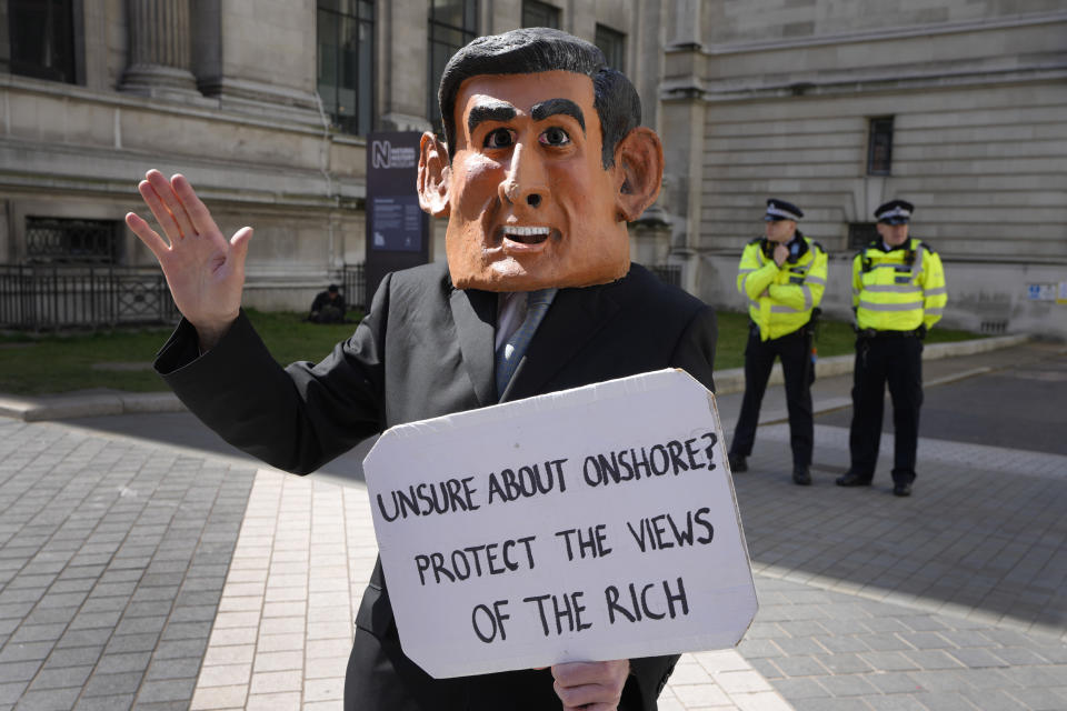 A climate demonstrator dressed as Britain's Chancellor Rishi Sunak holds up a placard outside the Natural History Museum as Extinction Rebellion continues a week of action and outreach in London, Monday, April 11, 2022. (AP Photo/Kirsty Wigglesworth)