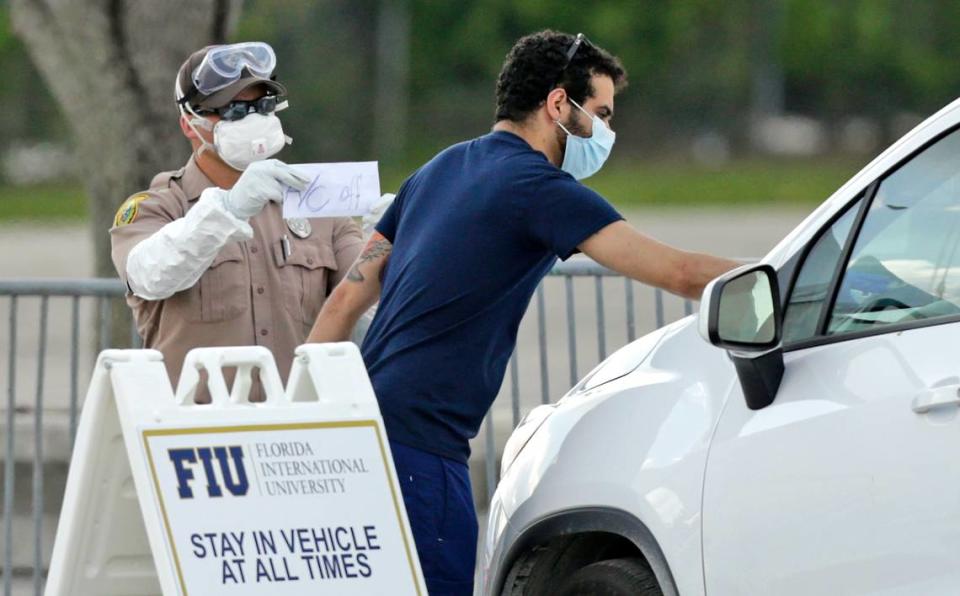 A healthcare worker helps to check in with the assistant from Miami-Dade police as vehicles line up at the COVID-19 drive-thru testing center at Tamiami Park on Wednesday. A drive-thru testing site to open next week in Aventura will use pin-prick blood tests instead of nasal swabs.