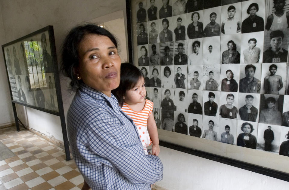 FILE - In this Feb. 12, 2009, file photo, a local woman holds her baby as she stands next to portraits of former prisoners on display at a the notorious former Khmer Rouge prison, S-21, now the Tuol Sleng genocide museum, in Phnom Penh, Cambodia. The Khmer Rouge’s chief jailer, who admitted overseeing the torture and killings of as many as 16,000 Cambodians while running the regime’s most notorious prison, died at a hospital in Cambodia early Wednesday morning, Sept. 2, 2020. Kaing Guek Eav, known as Duch, was 77 and had been serving a life prison term for war crimes and crimes against humanity. (AP Photo/Heng Sinith, File)