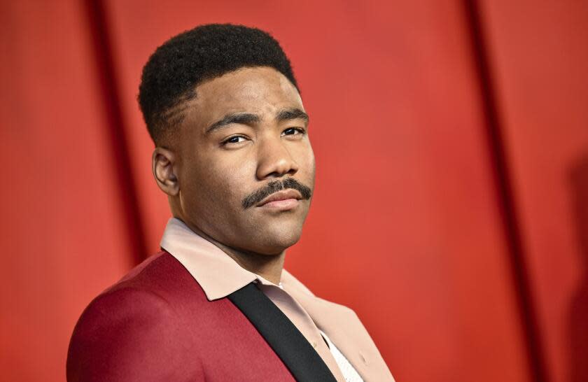 Donald Glover poses in a red suit in front of a red background