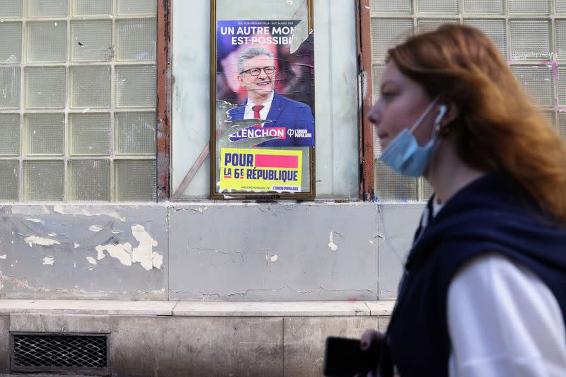 A young woman walks past an official campaign poster of French far-left leader Jean-Luc Melenchon in Aubervilliers