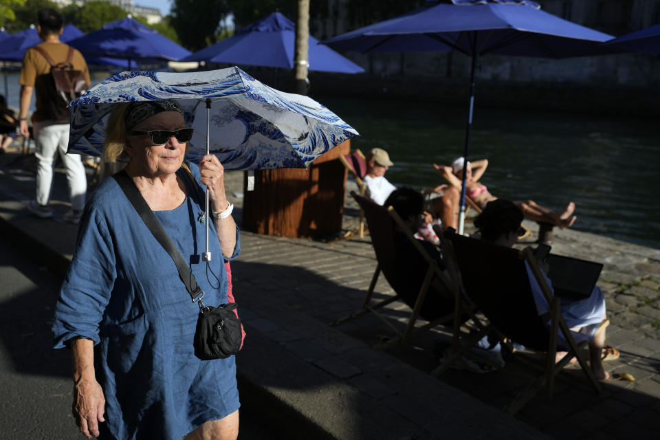 FILE - A woman shelters from the sun with an umbrella along the Seine River, as Europe is under an extreme heat wave, in Paris, France, Aug. 2, 2022. Food prices and overall inflation will rise as temperatures climb with climate change, a new study by an environmental scientist and the European Central Bank found. (AP Photo/Francois Mori, File)