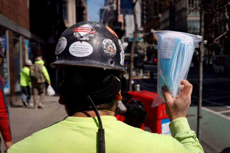 Construction worker holds up package of surgical masks at vendor on a street corner during outbreak of coronavirus disease (COVID-19) in New York