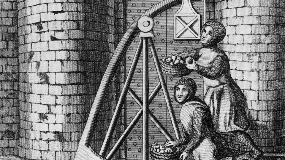 Around 1400, soldiers in chain mail loaded baskets of stones onto a trebuchet behind the walls of a castle.  (Hulton Archive/Getty Images)