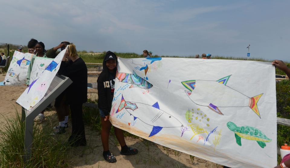 Provincetown school students greet arriving guests with their artwork at Herring Cove Beach in Provincetown on Thursday, World Ocean Day, for the unveiling of a shark sculpture made entirely of washed-up marine plastic trash.
